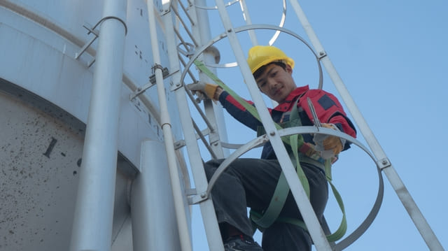 คนงานกำลังประเมินความเสี่ยงในการทำงานบนที่สูง กำลังคล้องสายช่วยชีวิตกับบันได